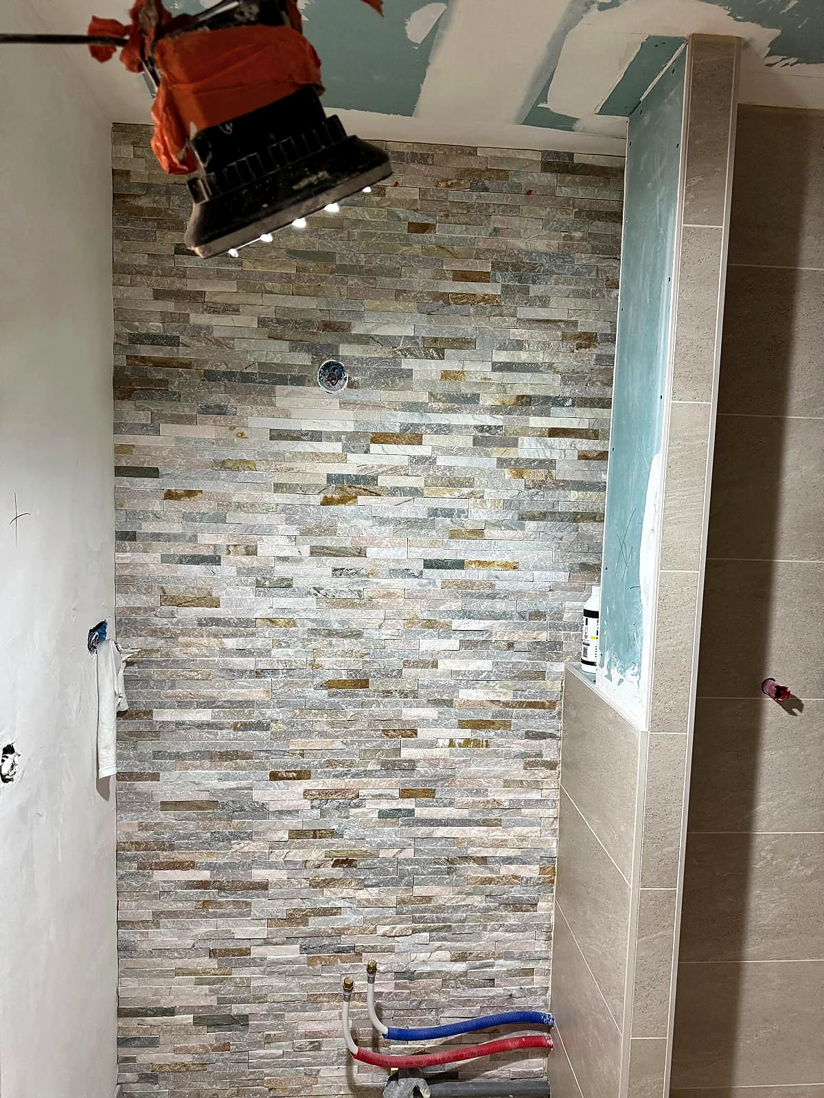 Chantier en cours de pose de carrelage mural effet pierre naturelle dans un espace douche